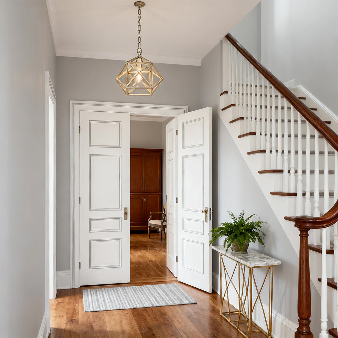 Gold metal pendant light hanging in a hallway with a white staircase, illuminating a marble console table for a luxurious look.