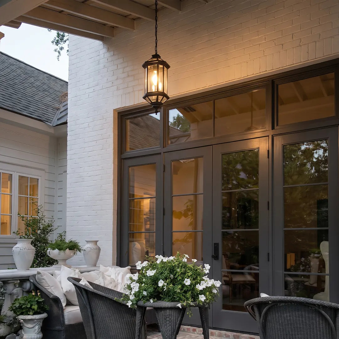 Hanging outdoor pendant lights over a covered patio entrance with black framed doors and outdoor seating.