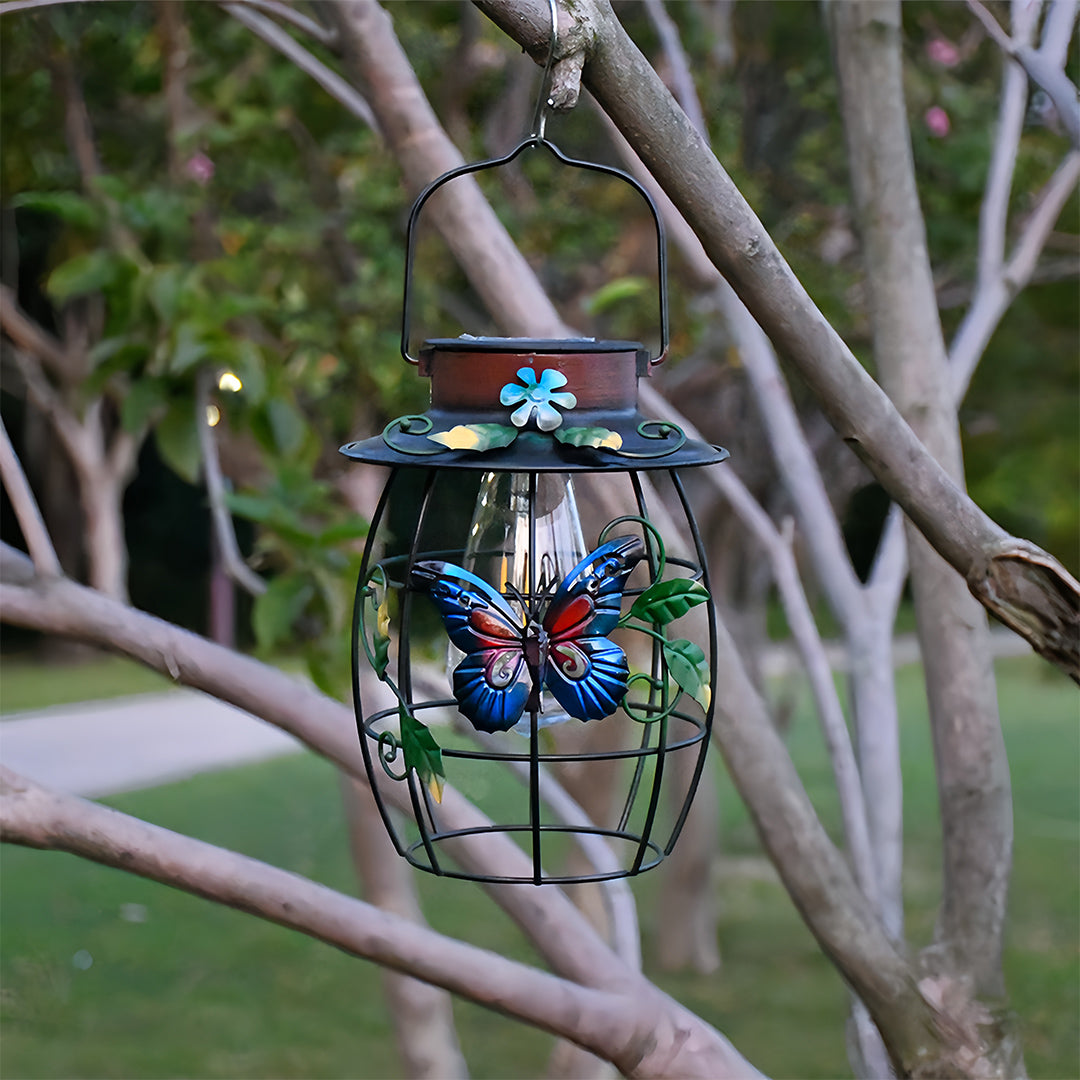Hanging solar iron outdoor lanterns with blue butterfly detail on a garden tree branch in daylight.