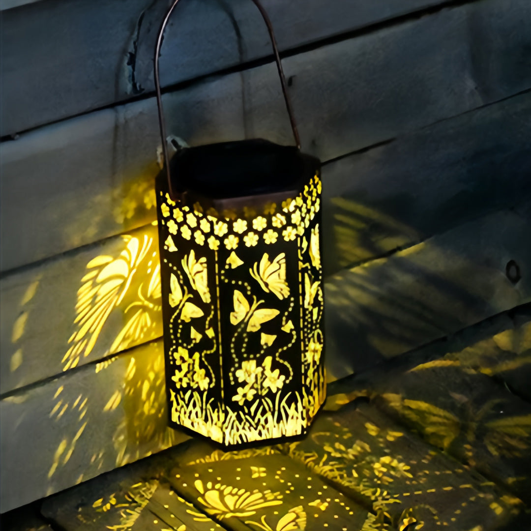 Hexagonal red outdoor lantern with floral cutouts casting intricate shadows on a wooden deck.