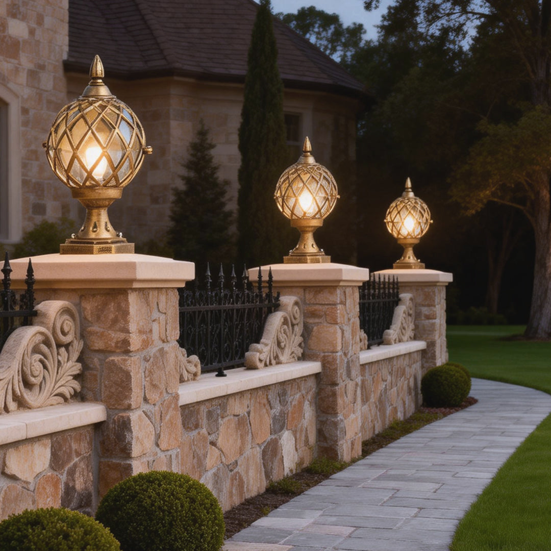 Classic home pillar light featuring a gold lattice sphere, installed on a stone fence along a garden pathway.