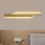 Horizontal overlap linear led wall light with a gold finish and light wood paneling, mounted above a bed in a contemporary room.