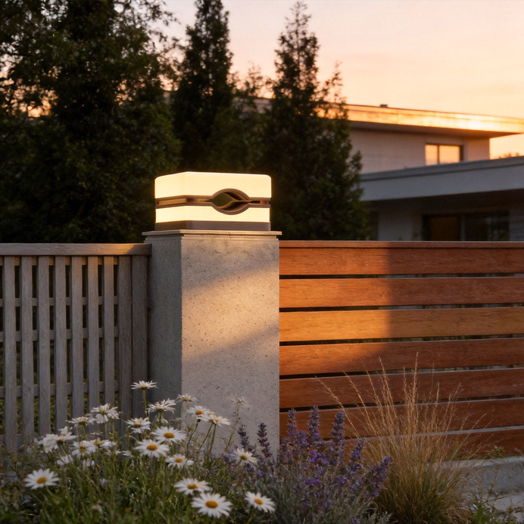 House pillar lights illuminating a modern house entrance with a black metal fence and stone pillars.