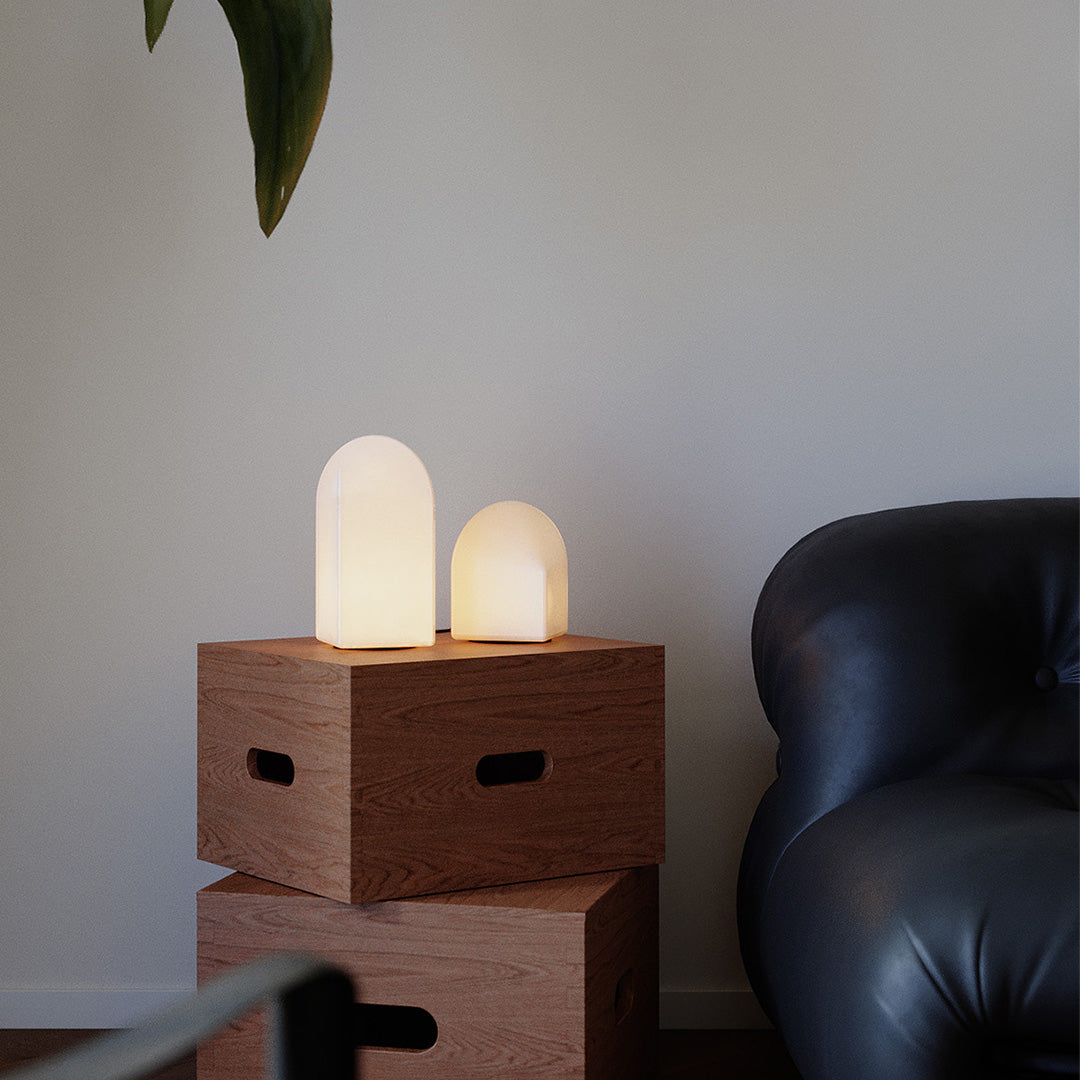 Two house-shaped modern white table lamps on wooden boxes beside sofa.
