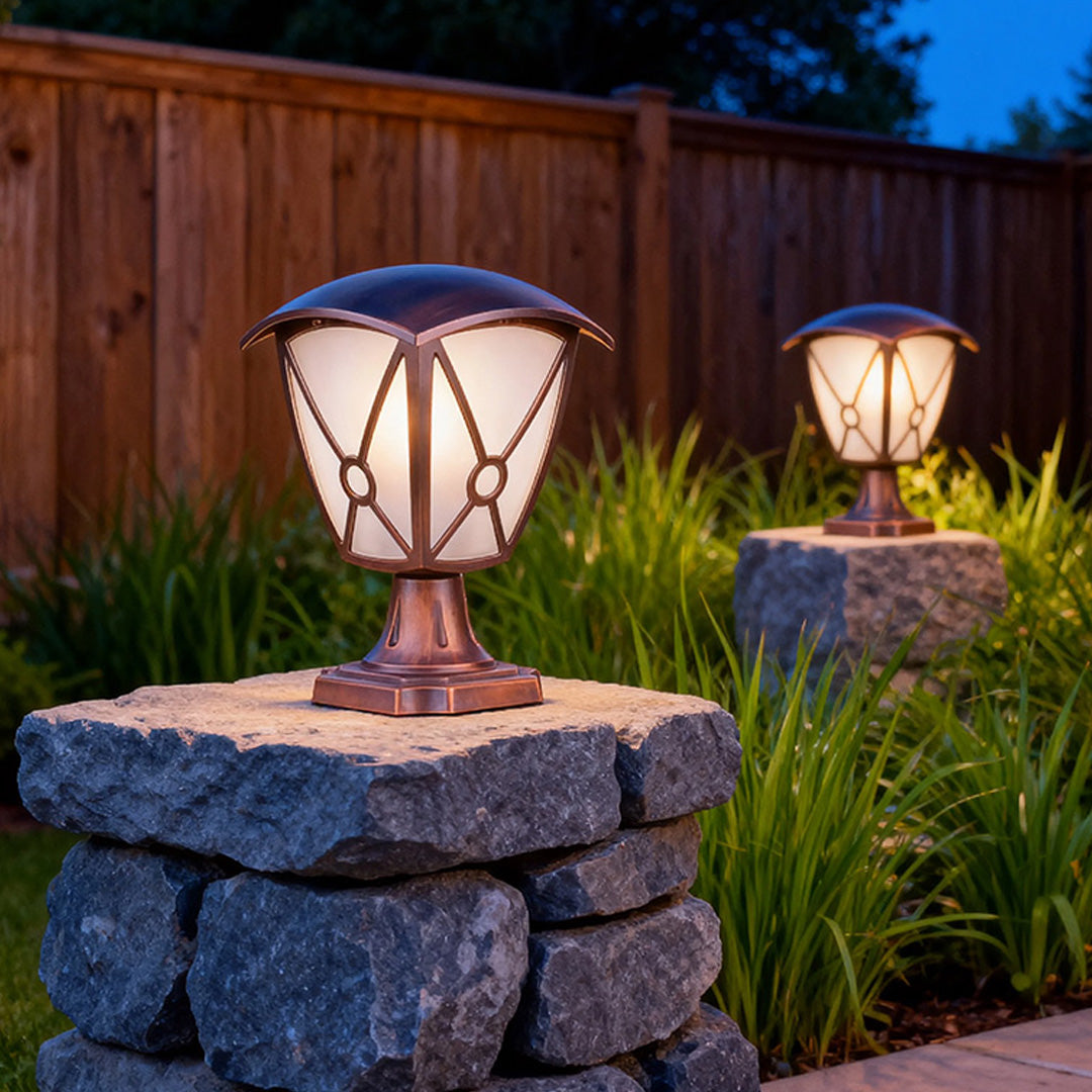 Illuminated aluminum pillar light mounted on stacked stone pillars beside wooden fence at dusk