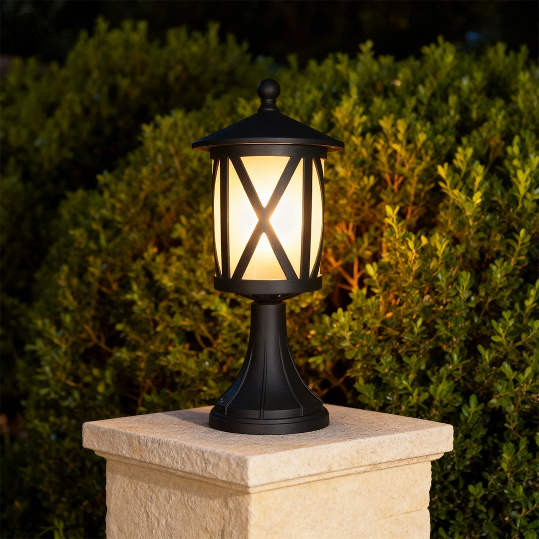 Illuminated black outdoor pillar light mounted on beige stone column in evening garden with dark backdrop