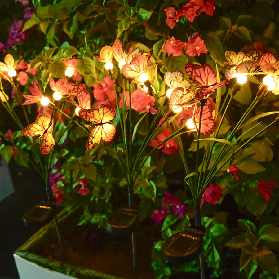 Illuminated butterfly flower lights creating magical glow among garden plants at night
