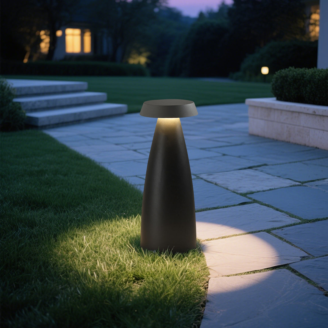 Illuminated black conical bollard light casting a warm glow in a modern outdoor setting.