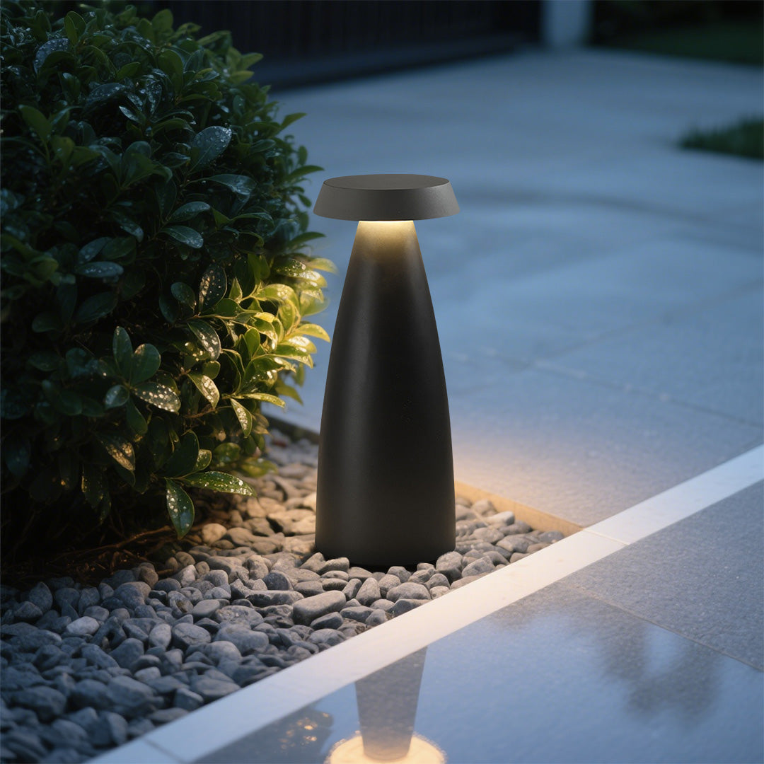 Black conical bollard light illuminating a gravel pathway in a landscaped garden.