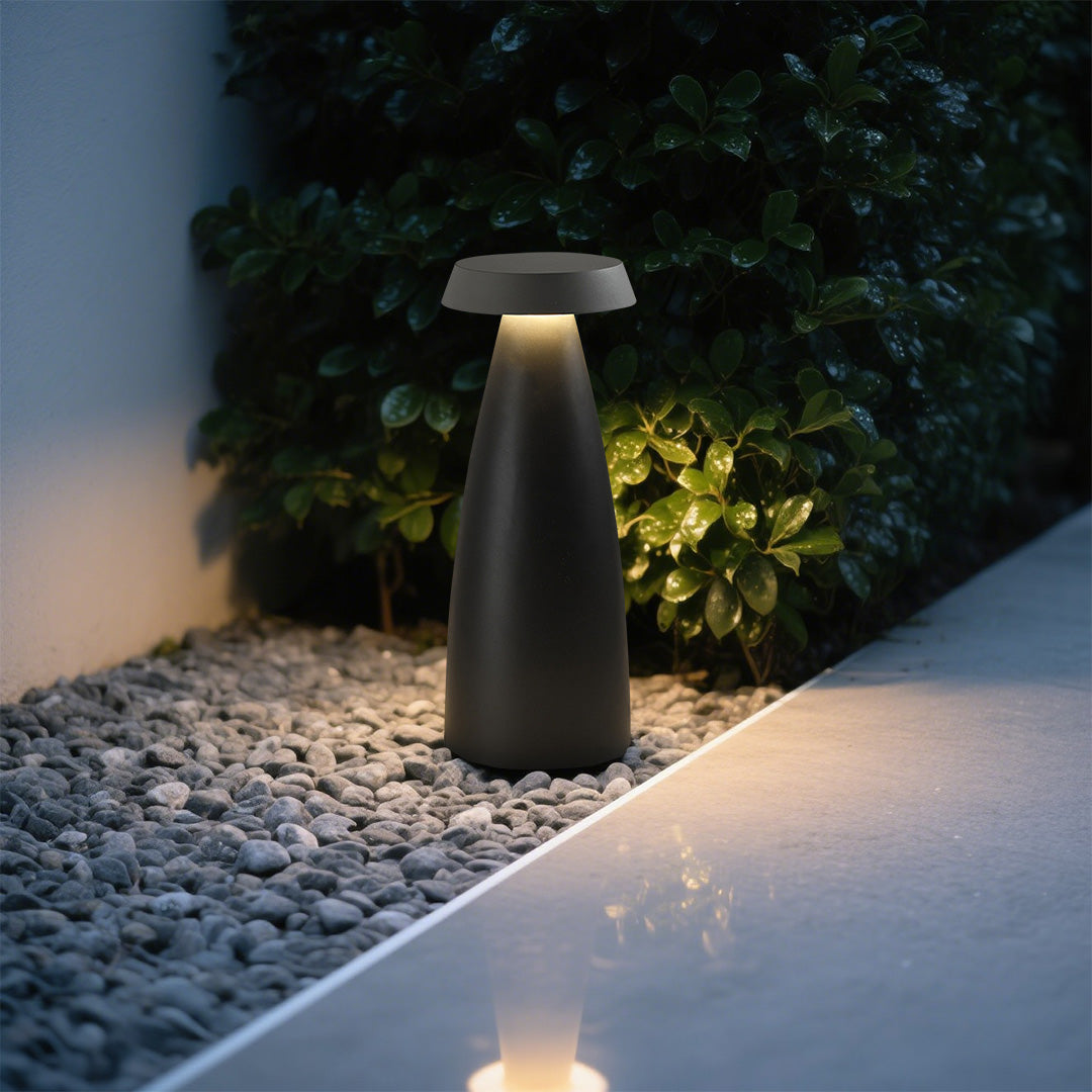 Black conical bollard light illuminating a gravel pathway in a landscaped garden.