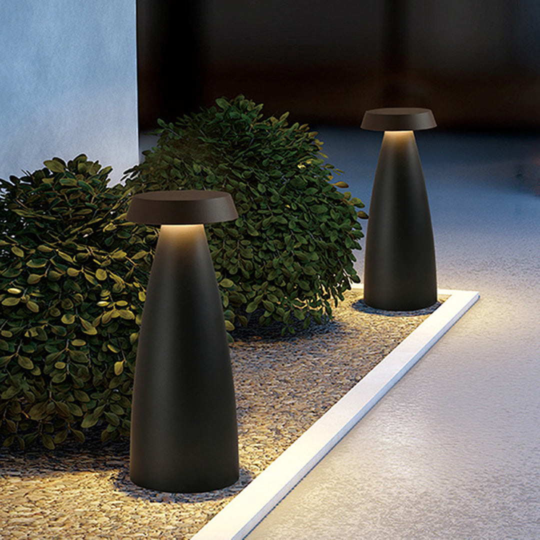 Black conical bollard light illuminating a gravel pathway in a landscaped garden.