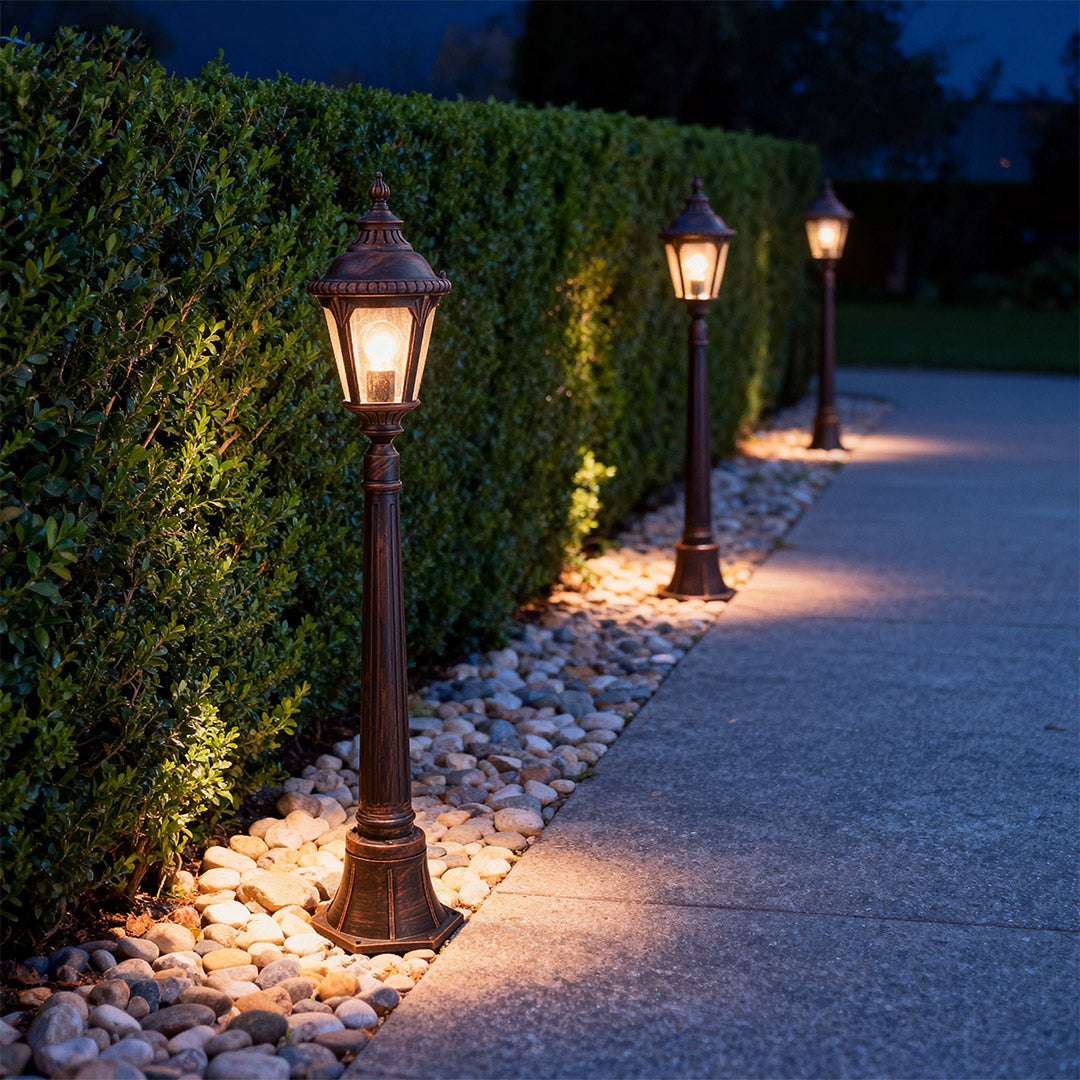 Illuminated decorative bollard light glowing warmly along mulched pathway at night with evergreen backdrop