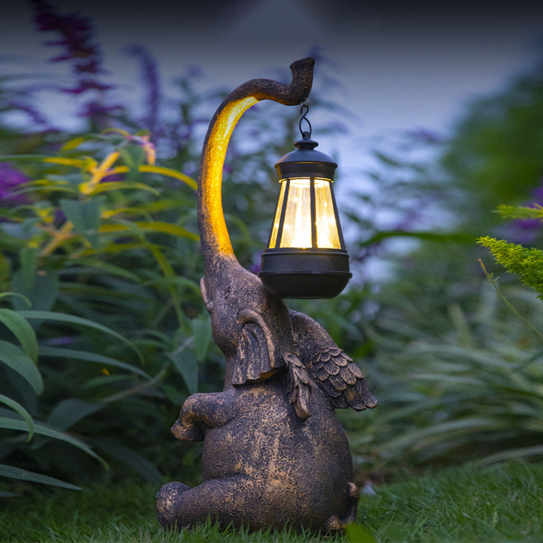 Illuminated elephant lantern holder glowing warmly in evening garden setting with plants