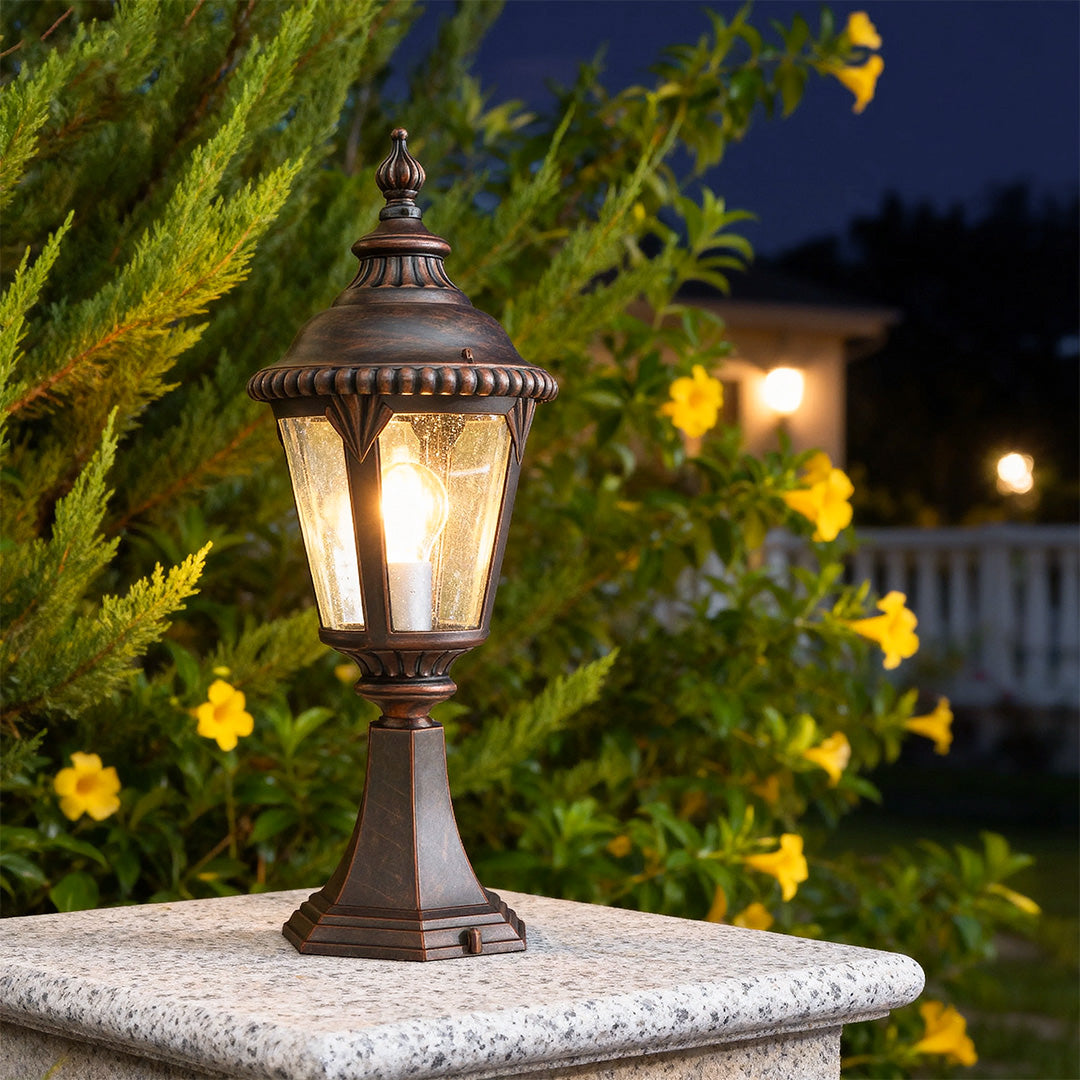 Illuminated fence pillar light glowing warmly on white stone column at dusk with foliage