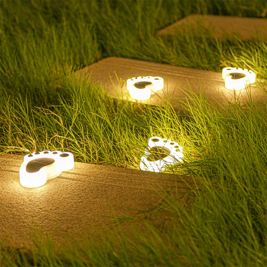 Illuminated foot-shaped solar garden lights providing gentle lighting on grass lawn surface