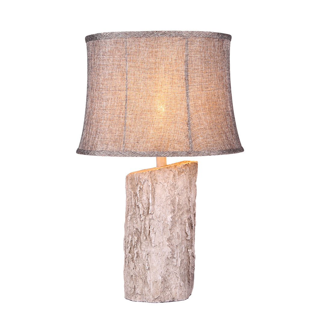 Full-view product shot of the illuminated white wood table lamp, highlighting the light passing through the rustic woven shade material.