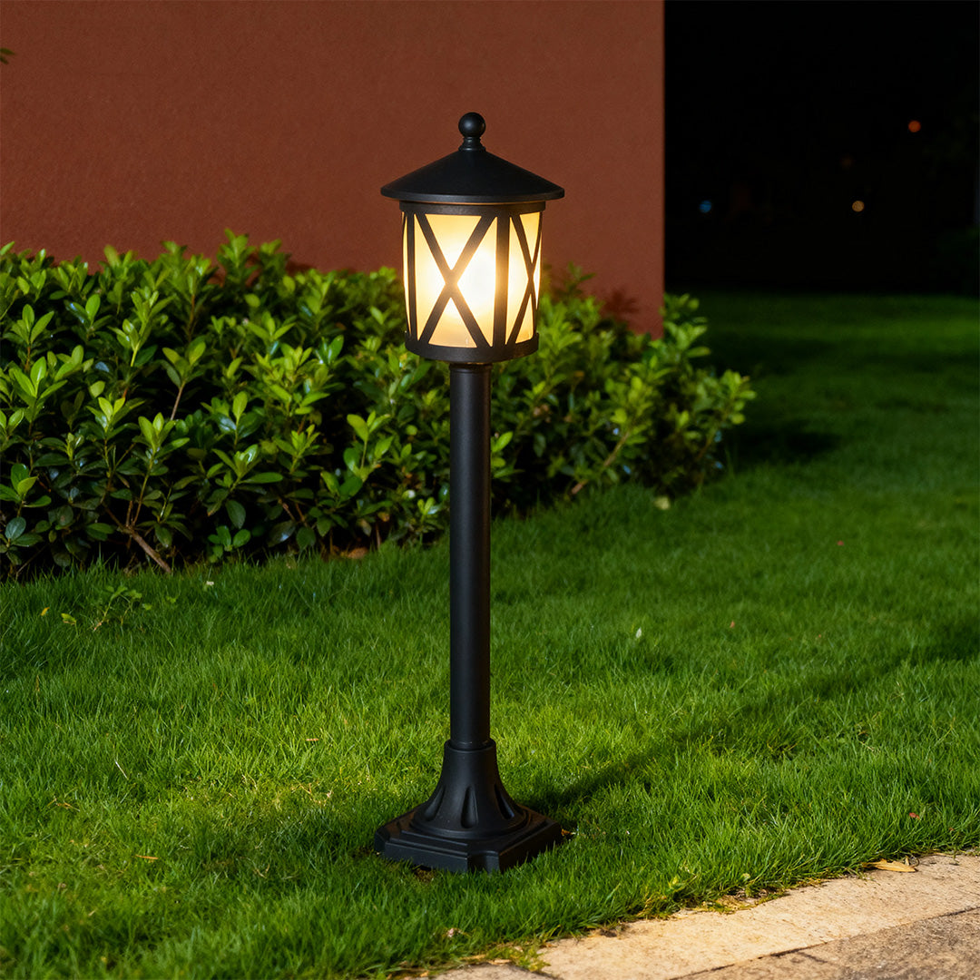 Illuminated garden bollard light casting warm glow on green lawn beside brown wall at night