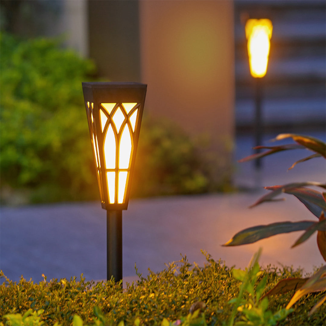 Illuminated garden torch light with geometric pattern casting warm glow on plants