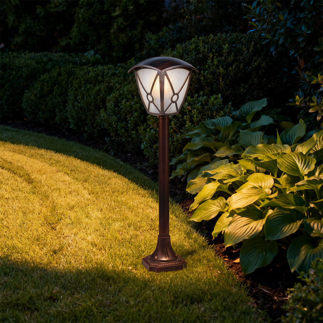 Illuminated LED fence bollard light casting warm glow on golden evening lawn with dark trees