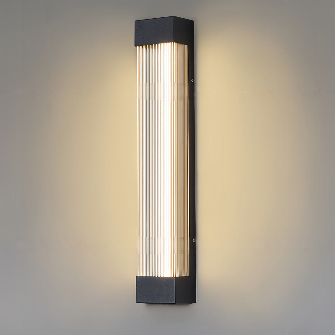 Illuminated linear outdoor sconce displaying its warm white light output against a plain grey wall.