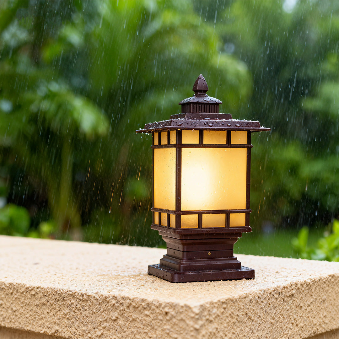 Illuminated metal pillar light with warm glow on stone pillar surrounded by lush tropical garden foliage