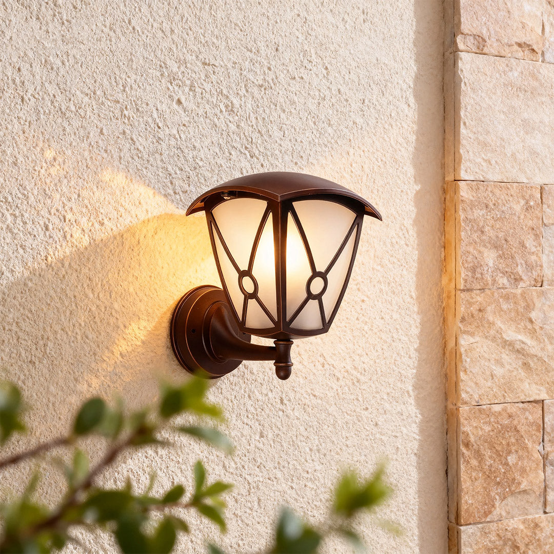 Illuminated outdoor wall light for house mounted on rough stone exterior with soft focus greenery