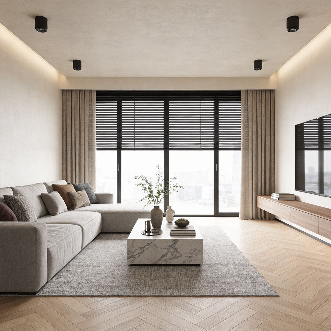 Indoor spotlight lamps illuminating a modern living room with a light beige sofa and large windows.