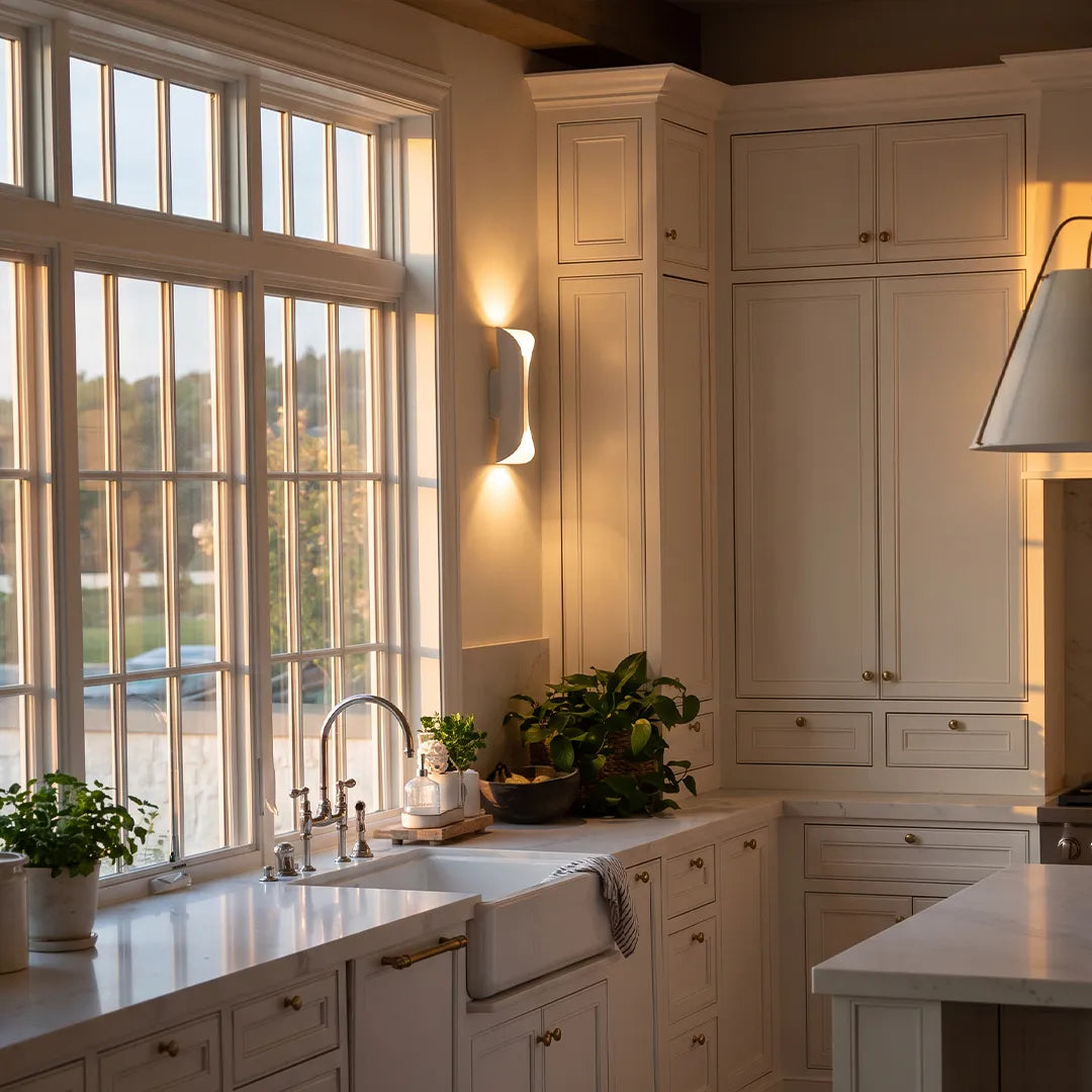 Indoor up down wall lights mounted in a bright kitchen, casting warm light beside tall windows.
