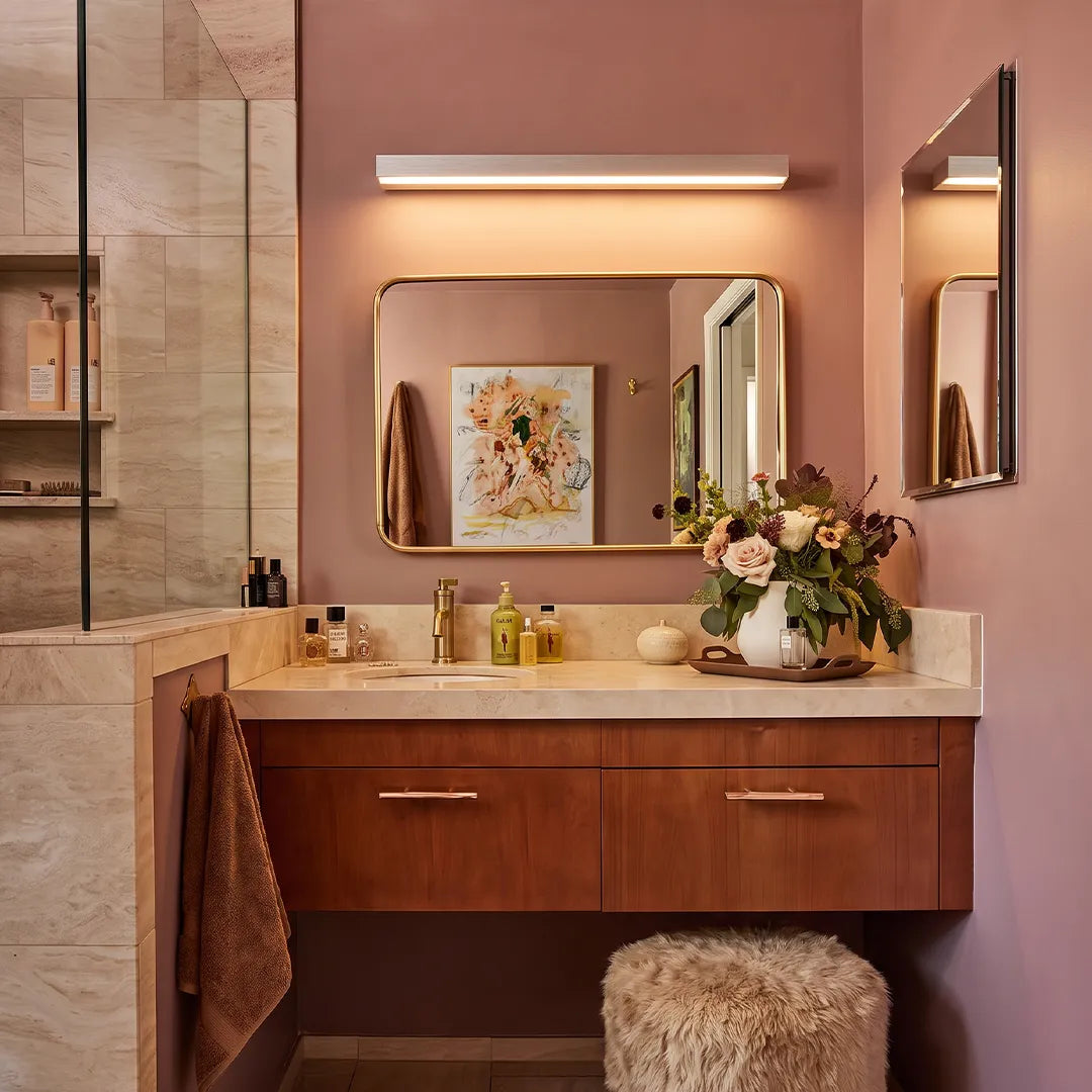 Indoor wall washer light installed above a bathroom mirror, paired with a wood vanity and warm mauve walls.