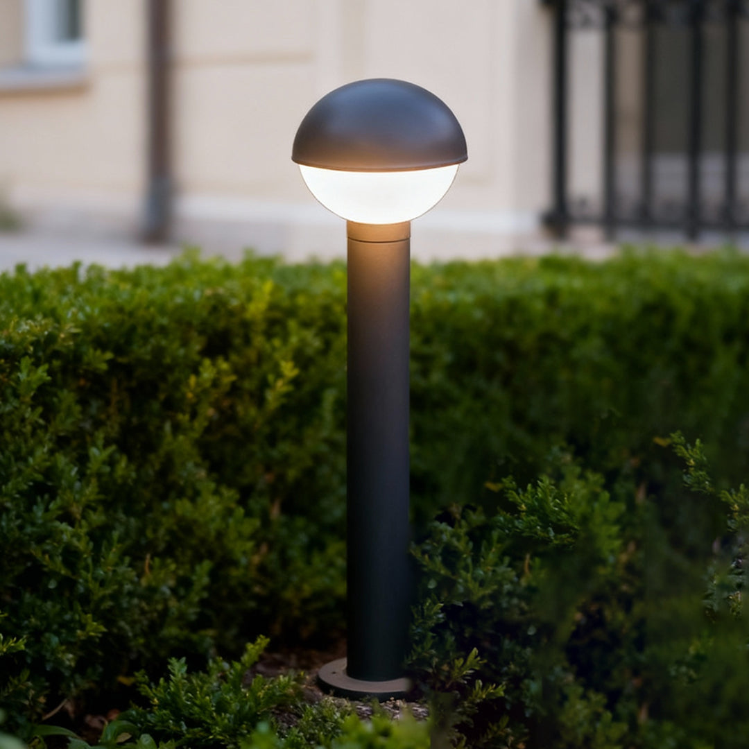 Industrial bollard lights with a rounded dome top illuminating pathway edges, creating a soft modern outdoor glow.