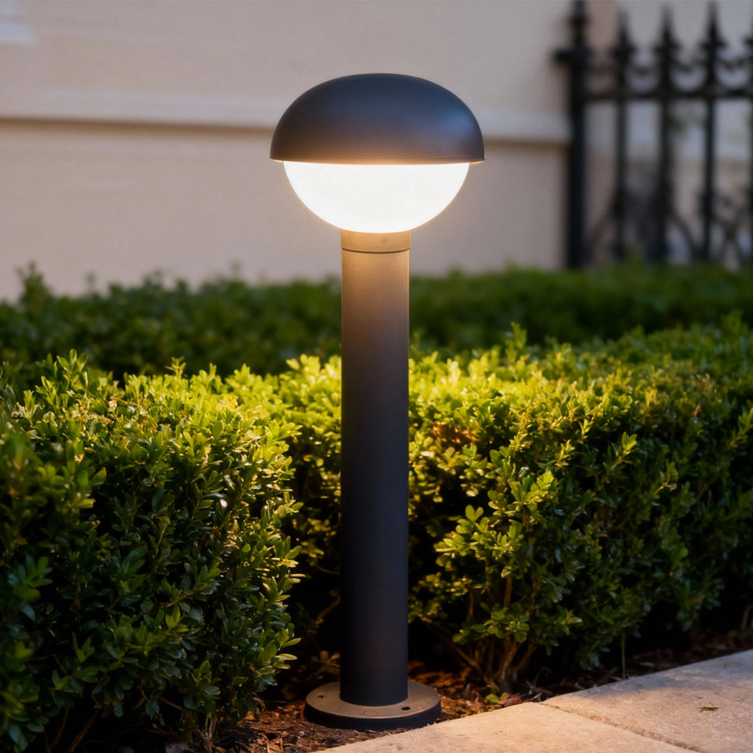 Industrial bollard lights installed along a garden hedge, featuring a rounded top and warm pathway lighting effect.