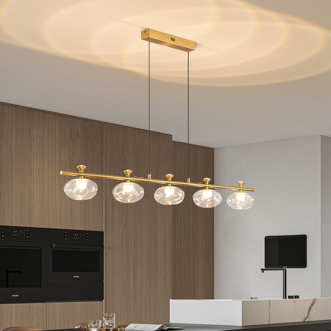 Industrial linear glass chandelier with brass accents positioned over modern dining table