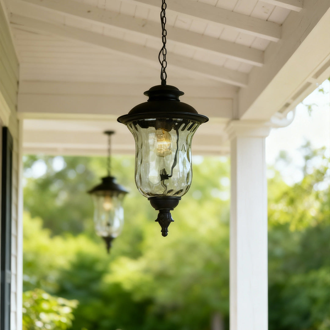 Industrial metal pendant light hanging from white porch ceiling with green landscape view