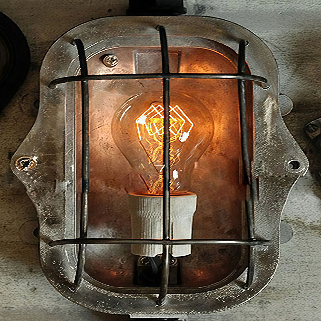 Industrial outdoor sconce with amber glass and metal grid illuminated against textured stone surface