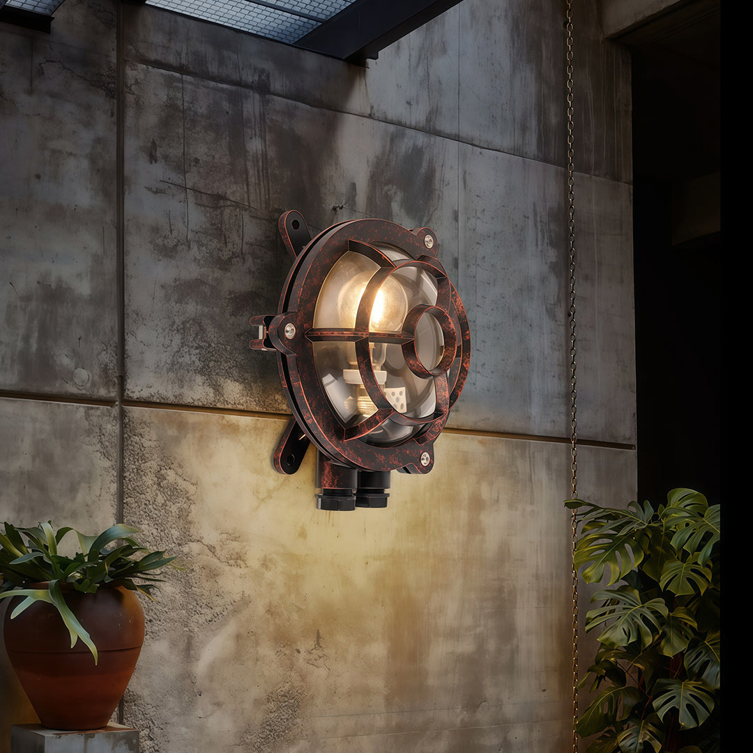 Industrial outdoor sconce illuminating concrete exterior wall with vintage maritime-inspired cage design at dusk