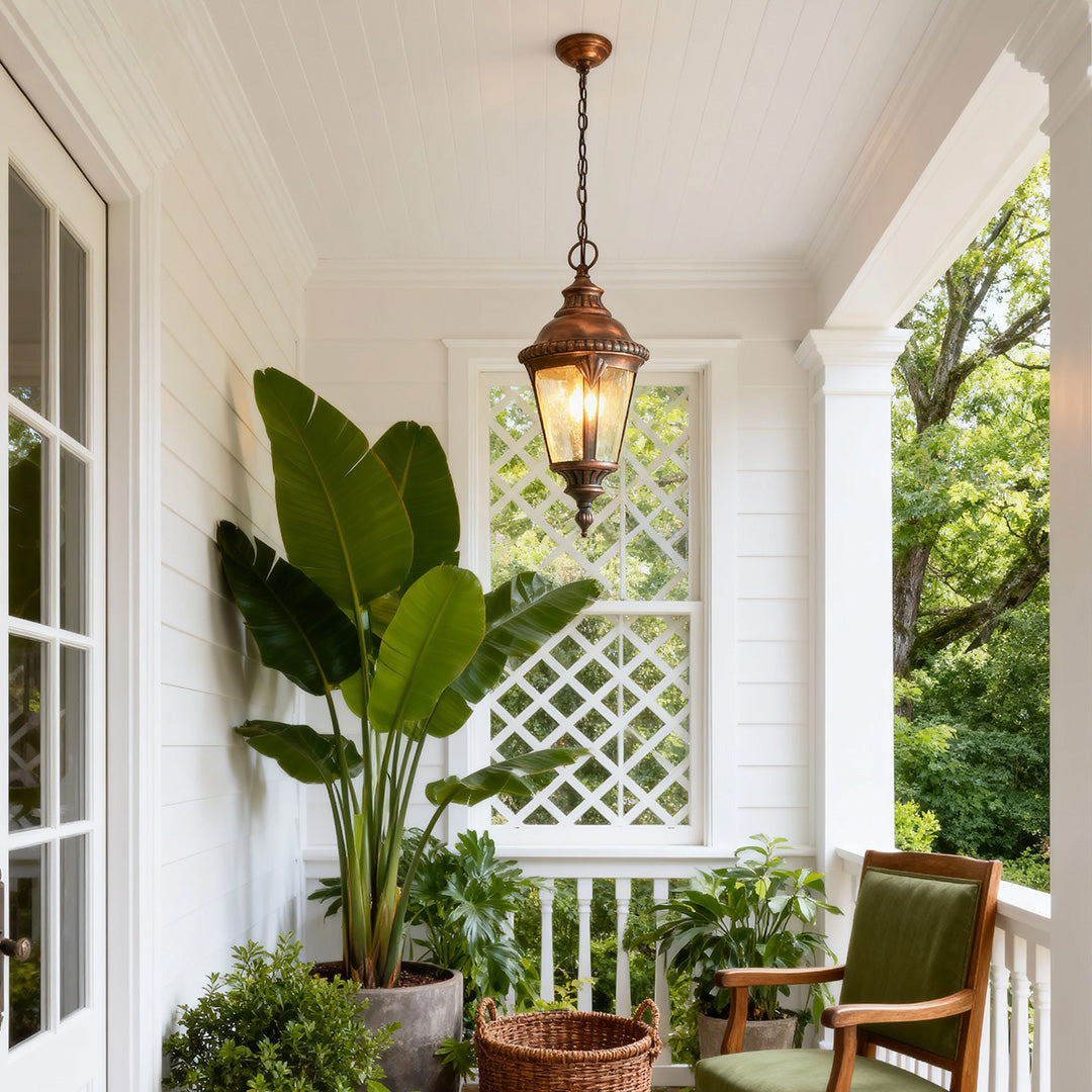 Industrial pendant light hanging in white covered porch with tropical plant and outdoor furniture