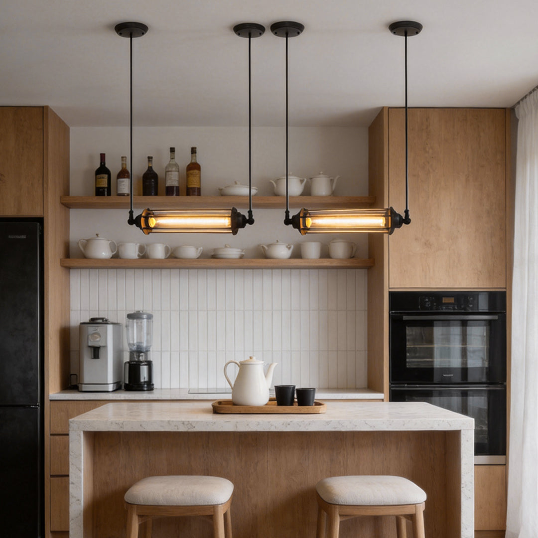 Industrial style pendant light fixtures with horizontal tube design suspended over a minimalist kitchen counter with warm ambient glow.