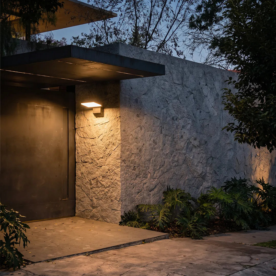 Industrial wall light illuminating a modern entry with textured concrete walls and a covered walkway.