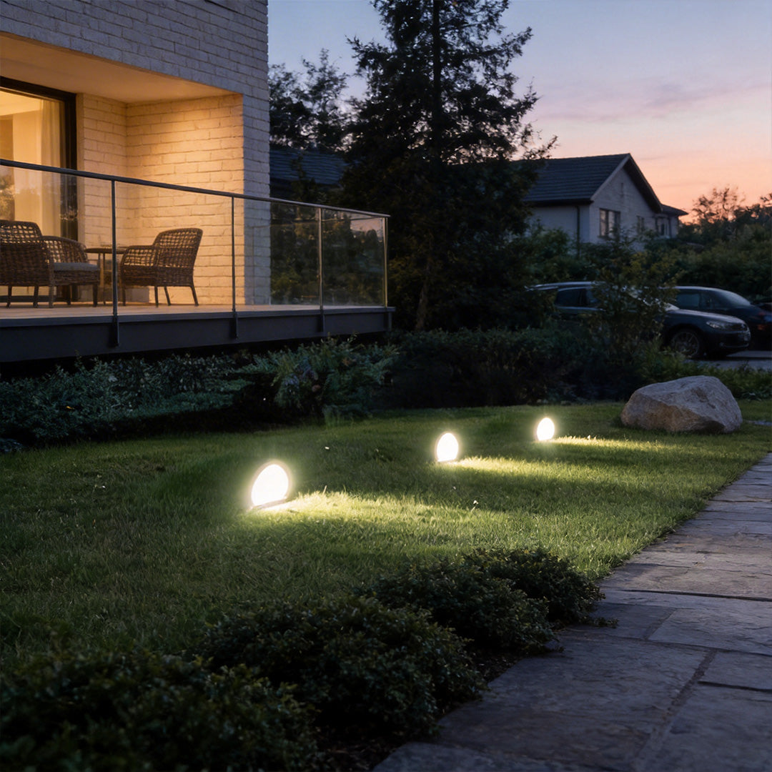Inground landscape lights with a warm glow, lighting up a modern house driveway.