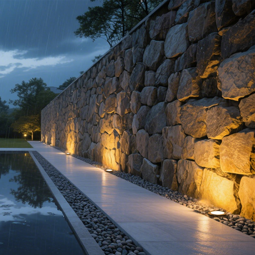 In-ground uplights creating dramatic illumination along stone wall pathway during evening hours