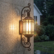 Vintage wall sconce lighting installed on an exterior wall with elegant bronze scroll details.