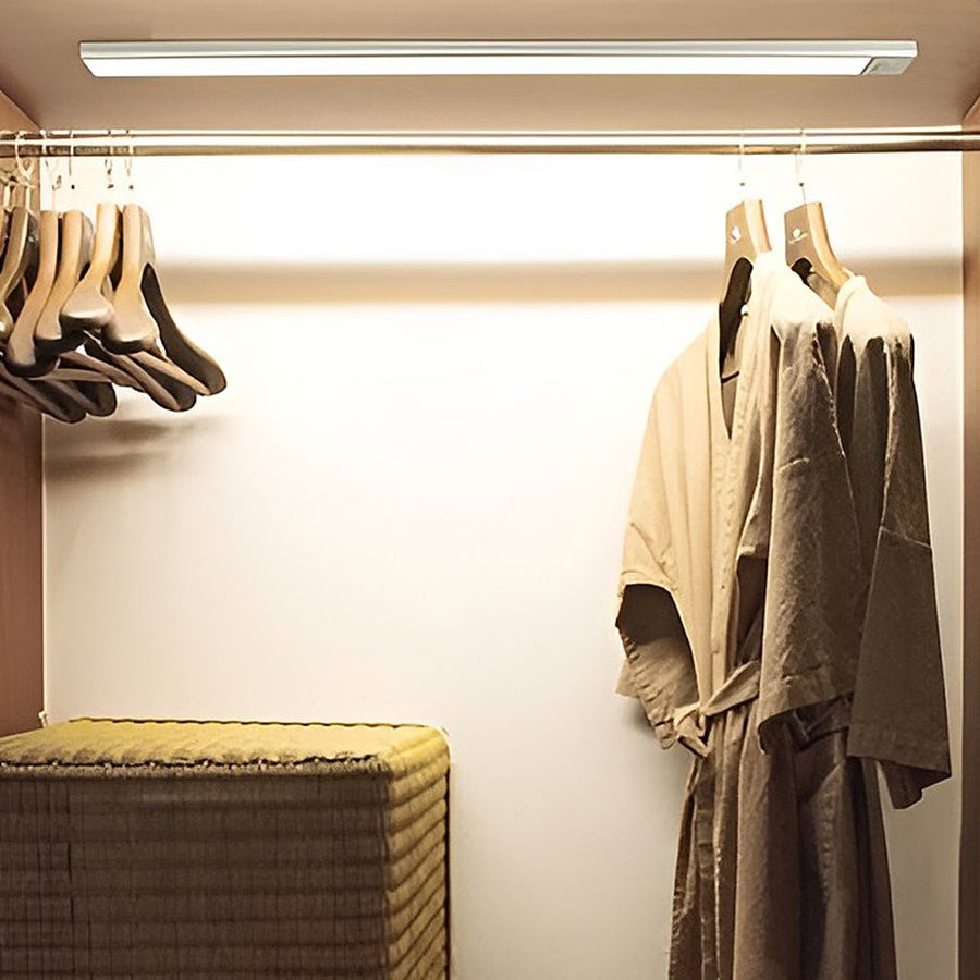 Efficient closet organization illuminated by bright wireless under cabinet lighting mounted above the clothes rail.
