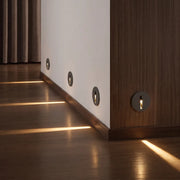 Interior stair step lights installed along a hallway wall, casting warm beams across a wood floor.
