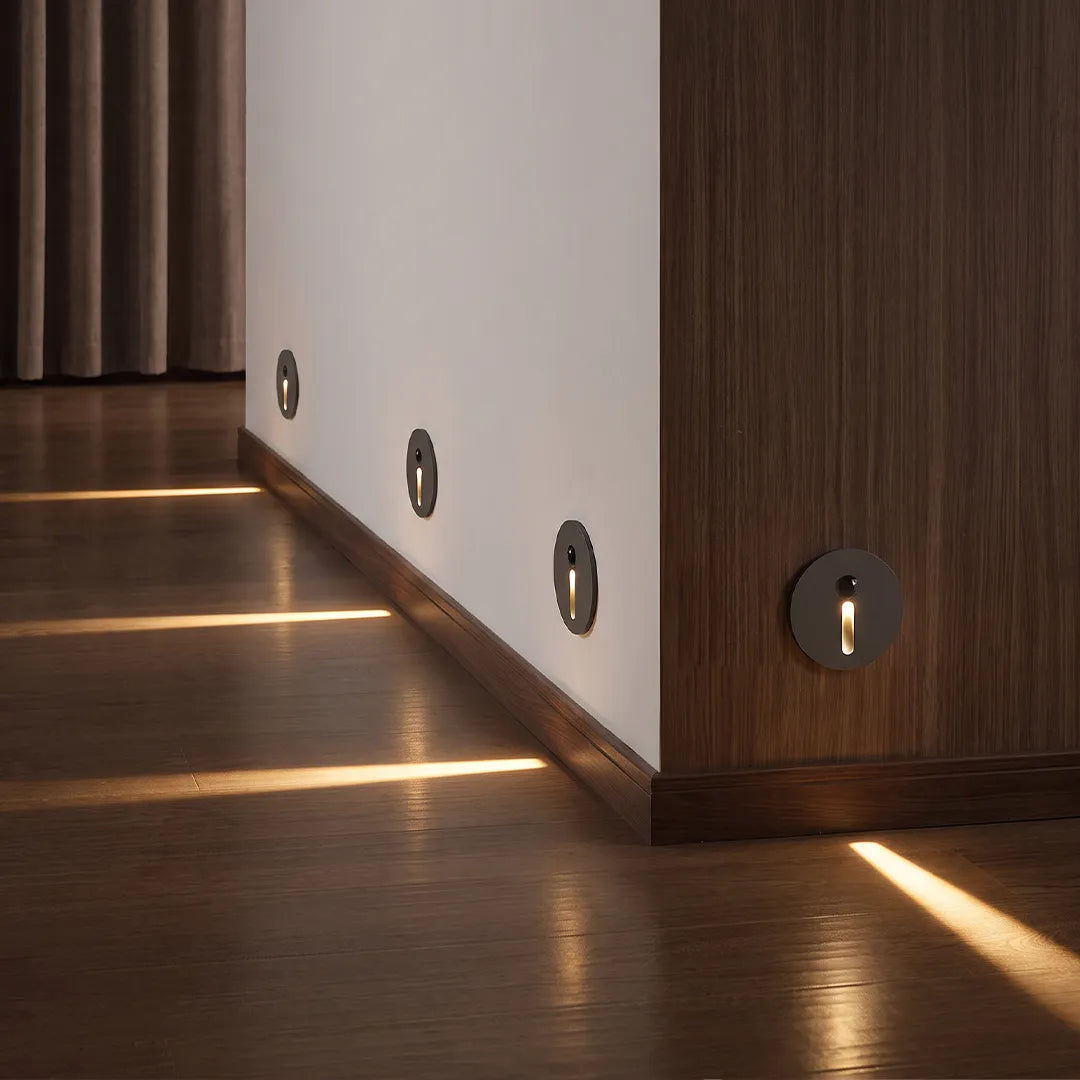 Interior stair step lights installed along a hallway wall, casting warm beams across a wood floor.