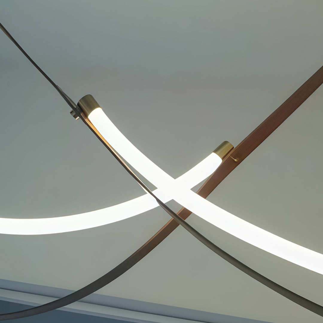 Intersecting neon pendant lights displaying sculptural design with copper accent element on grey backdrop.