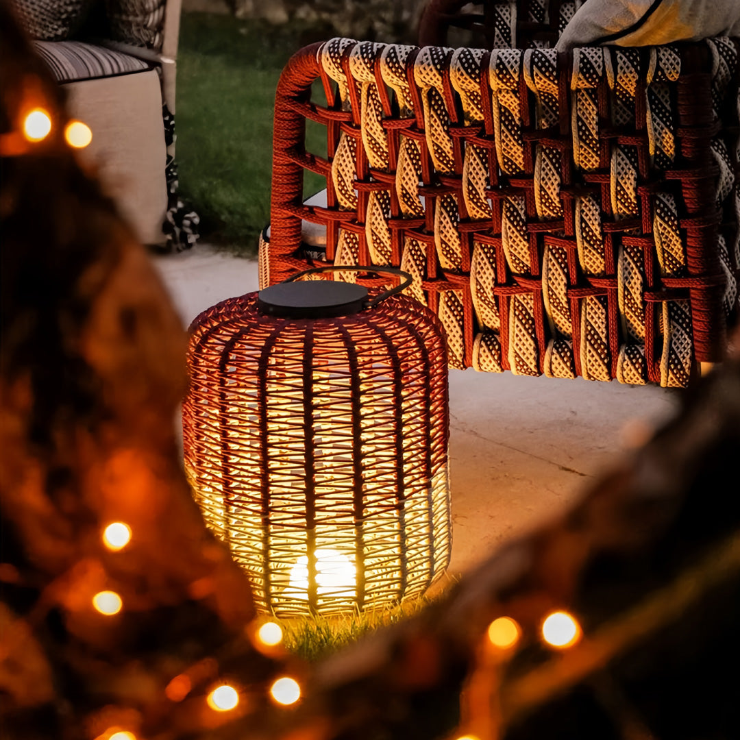 Close-up of a tall outdoor LED lantern base, showcasing the intricate red and brown woven pattern on a rough stone patio.