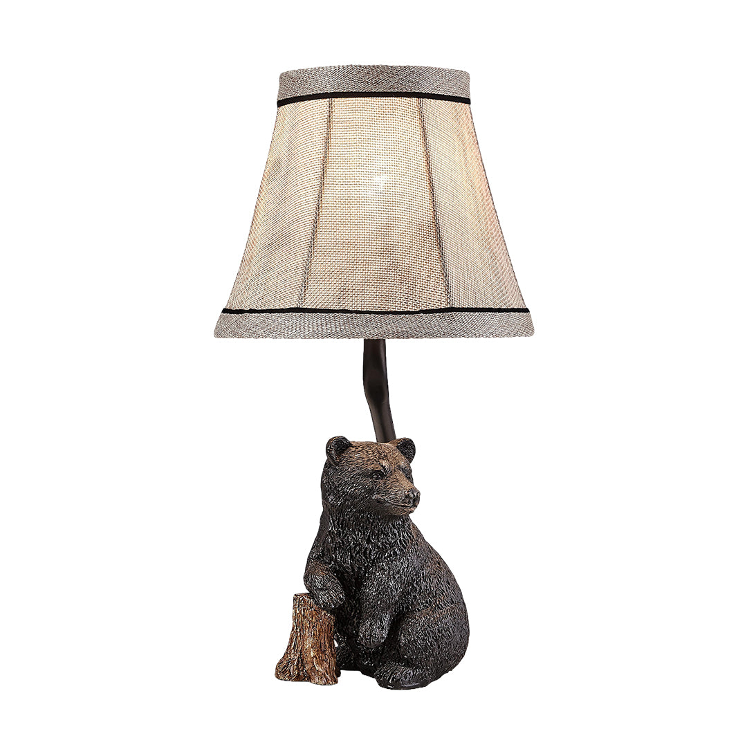 Isolated view of the rustic resin table lamp, showing the bear figure seated next to a log with a slight, warm glow from the bulb.