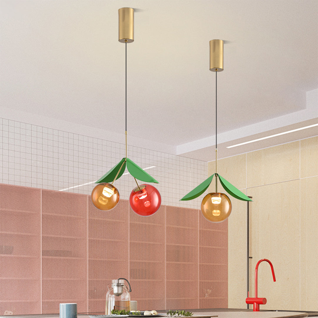Kitchen installation of glass globe pendant light fixture with fruit-themed design over pink tiles