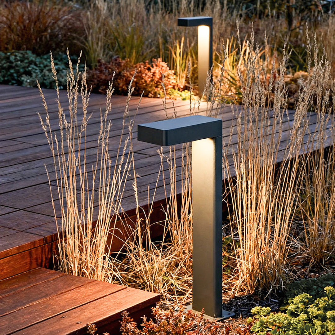 L shaped landscape light with a sleek black design, illuminating a garden pathway near plants.