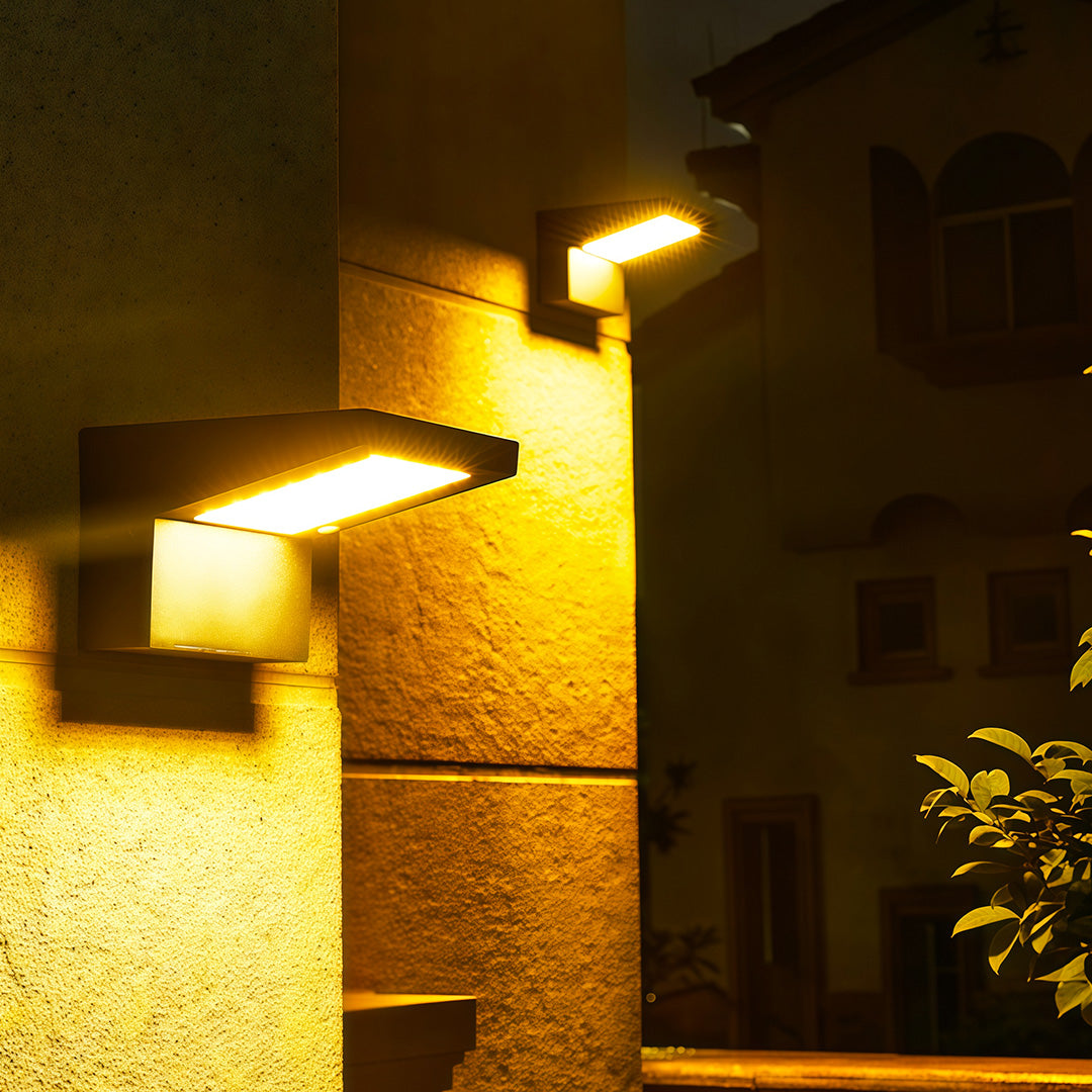 Warm yellow illumination from two L-shaped wall mount outdoor light fixtures on a building's corner at night.